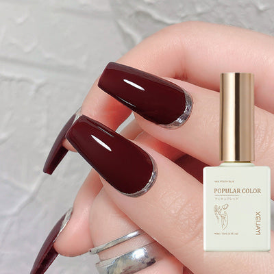 Durable wine red UV polish applied on long, glossy nails with decorative tips and polish bottle in view.