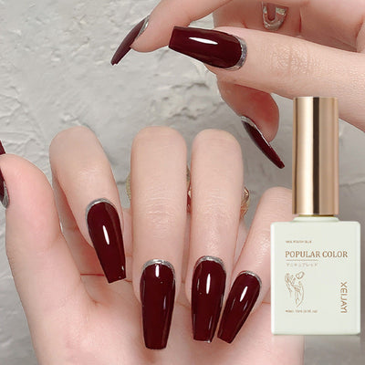 Durable wine red UV polish applied on long nails with elegant design and a bottle of popular color nail polish.